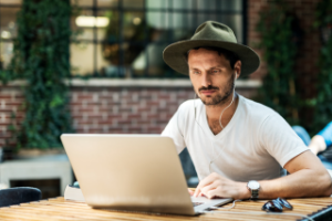 Mann med hatt sitter foran PC på café