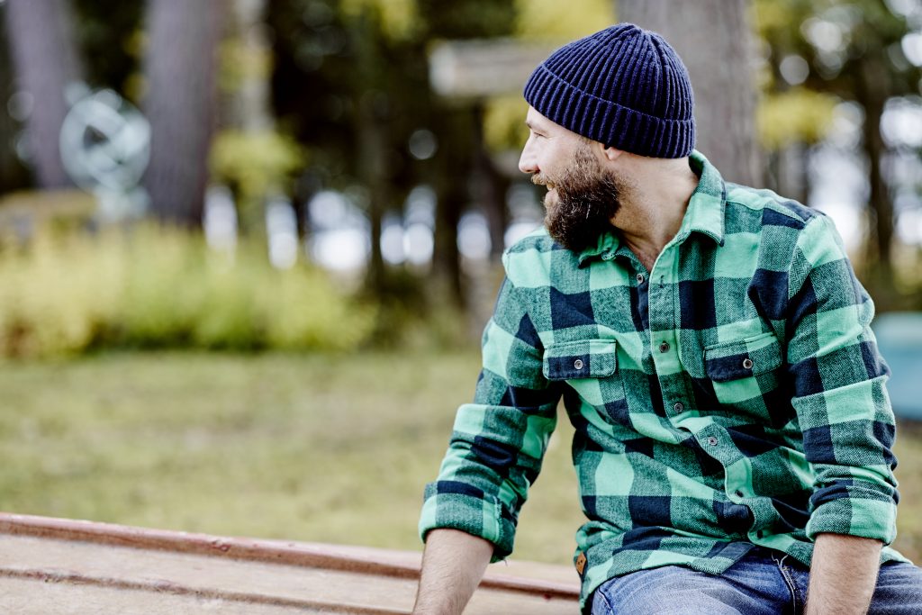 Mann sitter ute iført grønnrutete skjorte og blå lue