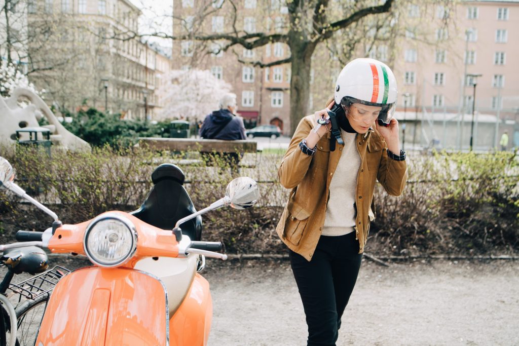 Ung kvinne med en moped ved en park