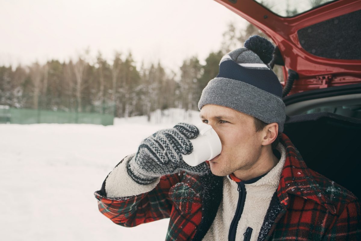 Mann drikker kaffe fra bilen på vinteren