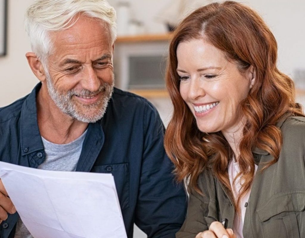 Et smilende par som sitter med pc og papir foran seg